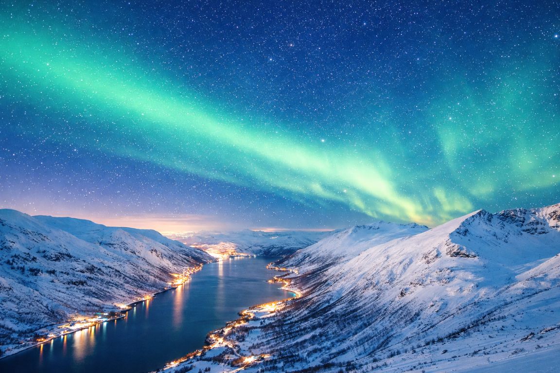 Northern Lights in Tromsø captured on a Tromso Norway Tours guided aurora excursion, featuring green aurora sweeping across a snowy fjord landscape at night