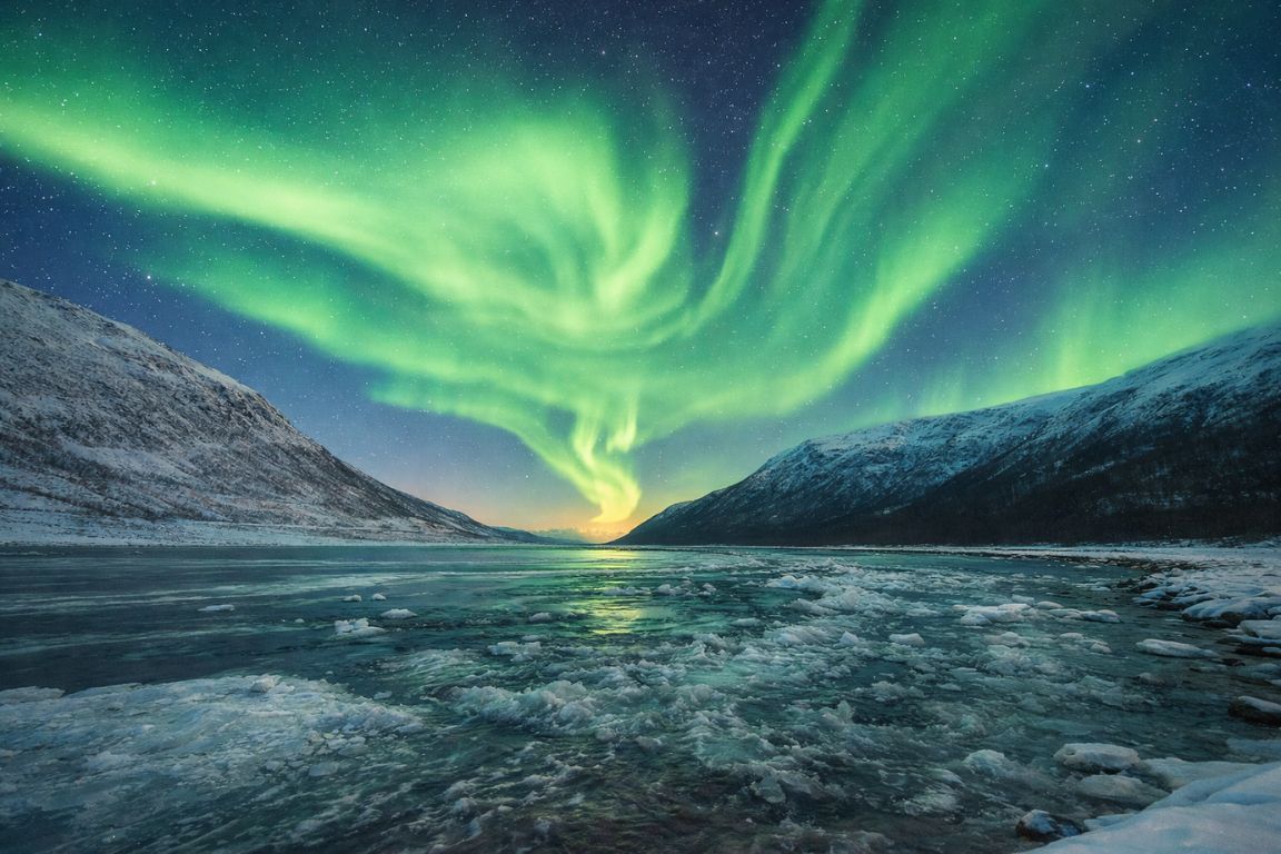Northern Lights over a frozen fjord in Tromsø photographed during a Tromso Norway Tours aurora tour, showing vivid green aurora above icy water and snow-covered mountains